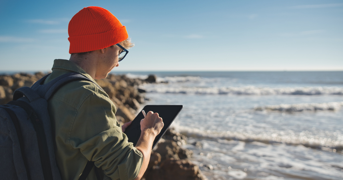 A marine biologist looks out to the ocean while working on a tablet.
